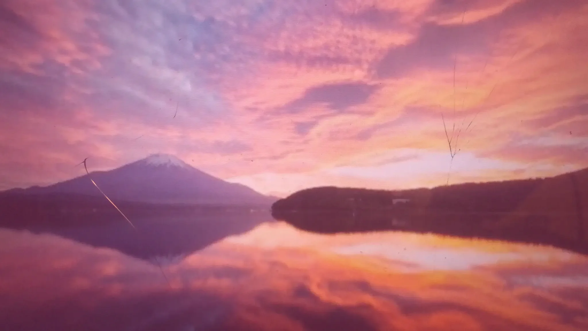 großer See mit einem Wald und Berg im Hintergrund, bei aufgehender Sonne